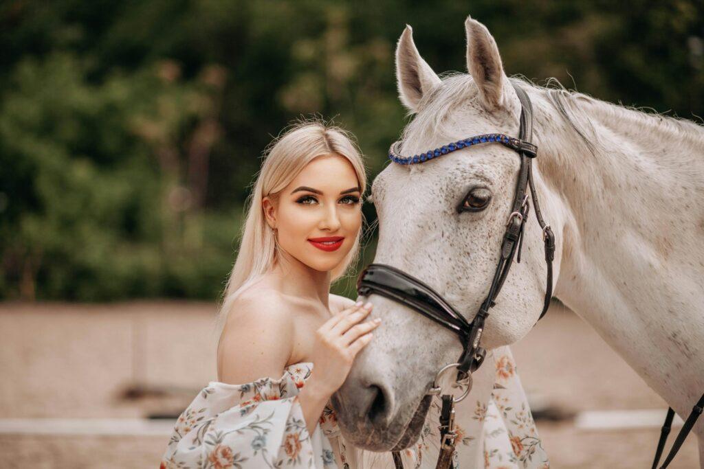 Beautiful woman posing with a white horse in a scenic outdoor setting.